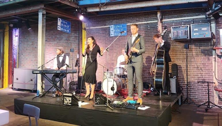 A music band including a woman singer, a pianist, a guitarist, a drummer, and a cellist